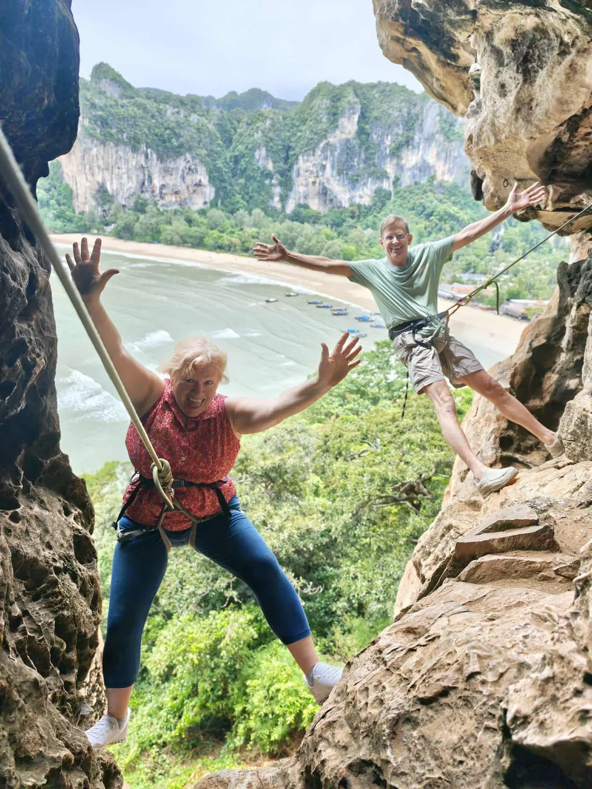 Two climbers with their arms up on a ledge high above Railay bay